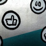 Buttons mit Daumen hoch, Smiley und Herz auf einer silbernen Wand