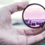 Hand im Vordergrund hält Vergrößerungsglas, mit dem man auf das Meer blicken kann