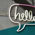 Sprechblase mit Schriftzug "hello" aus Leuchtröhren an einer Wand