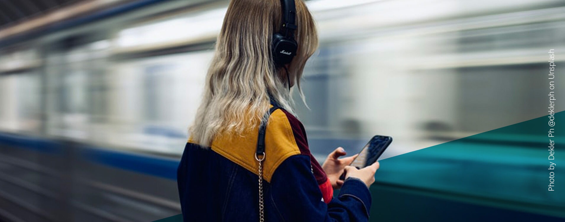 Frau mit blonden Haaren und Kopfhörern an einer U-Bahn-Station, durch die gerade eine Bahn fährt